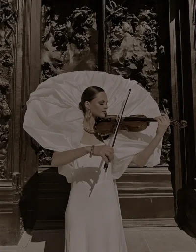 Galina Lanskaia jouant du violon en robe blanche, une ombrelle ouverte derrière elle