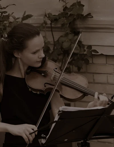 Galina Lanskaia jouant du violon en extérieur, contre un mur de pierre